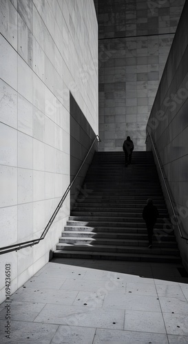 A striking black and white vertical view of anonymous figures ascending a long, modern concrete staircase, with harsh shadows creating a dramatic, minimalist architectural abstract