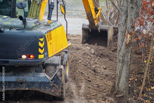Excavator digs soil with bucket at construction site with trees.