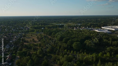 Aerial drone view of Sachsenhausen, Oranienburg, Germany, showing lush green forests, wetlands, ponds, and a railway line under a clear blue sky
