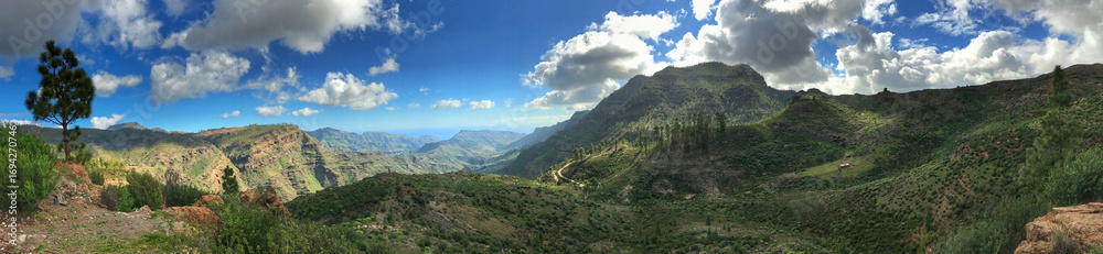 Naklejka premium Panoramic view of lush valley landscapes under a blue sky with clouds