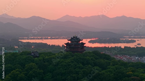 Aerial view of Chenghuang pagoda at sunset over Xihu lake in Hangzhou featuring mountains and lush green trees