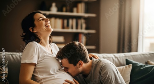 pregnant woman laughing with partner kissing her baby bump
