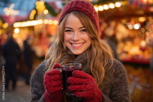 smiling woman in red gloves holding a hot drink, christmas market in the background