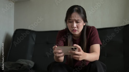 Stressed woman using phone and playing games while sitting on sofa at home and losing