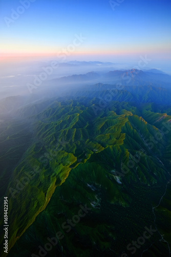 An aerial view of a lush mountain range bathed in the soft light of sunrise.