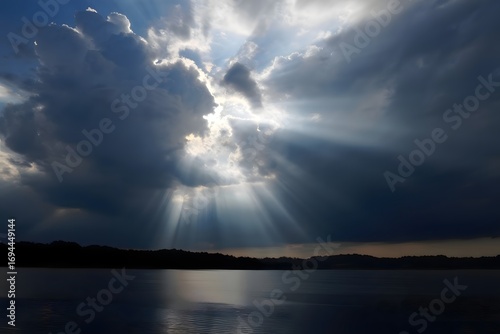 Wallpaper Mural Sun rays shining through dark clouds over a body of water with silhouetted trees in the distance Torontodigital.ca