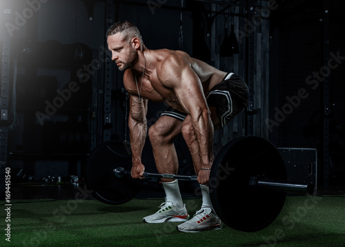 Muscular man training with weights. Brutal strong athletic men pumping up muscles workout in dark gym spotlight.