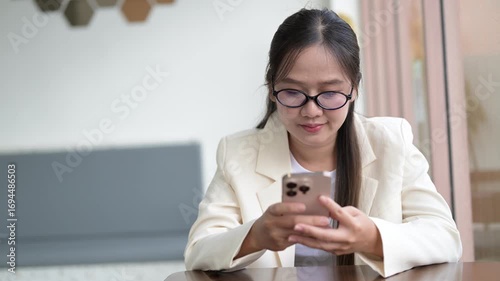Beautiful young businesswoman sitting on coffee shop using mobile phone while smiling and thinking looking through window during day