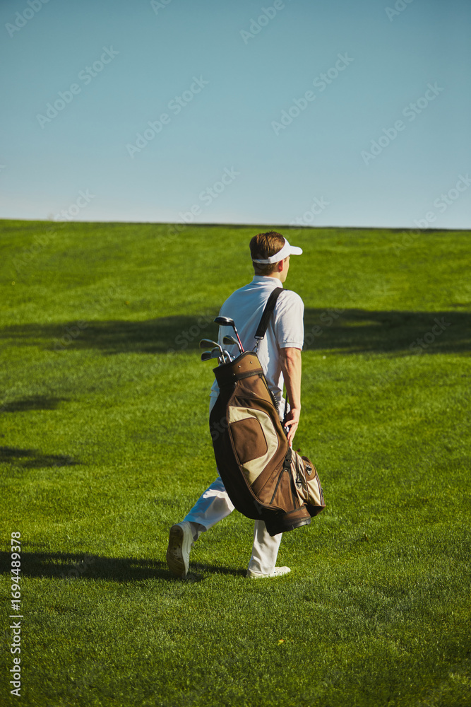 Obraz premium Golfer carrying bag walking across fairway on sunny day. Concept of sports lifestyle, leisure, health, outdoor activity, travel and wellbeing.