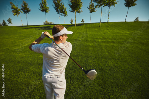 Fotografija Golfer swinging club on sunny green course with trees
