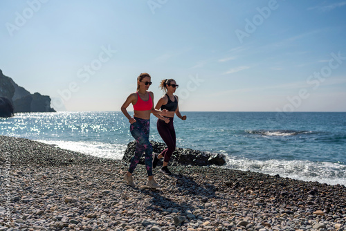 Slika na platnu Beach Running Fitness: Two women jog on sunny pebble beach for exercise, daytime cardio workout