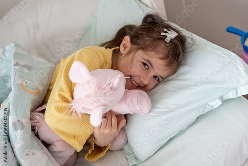 Morning awakening little child girl with her toy in bed. Happy girl in pajamas on bed right after awaking. Happy family concept