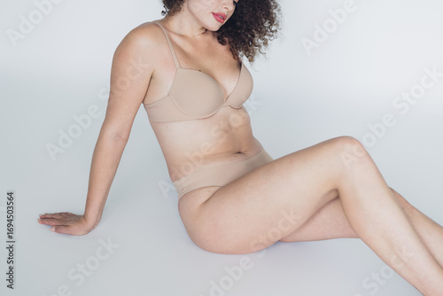 Fotografi Natural beauty of a young woman with curly hair in nude toned lingerie emphasizing confidence and self acceptance on a neutral backdrop
