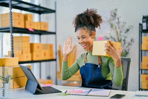 Online seller waving at customer during video call holding parcel in warehouse