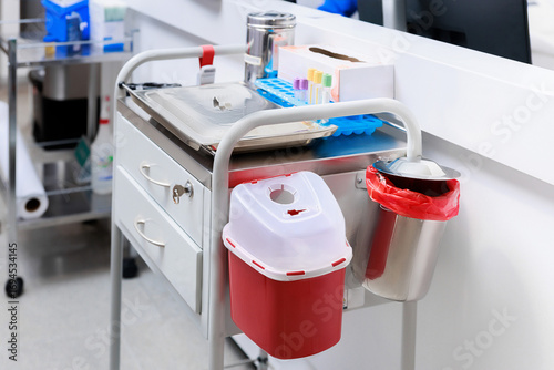Medical procedure cart with sharps container, test tubes, and sterile equipment in clinical setting