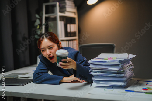 Foto Exhausted businesswoman yawning and holding coffee cup at office desk at night
