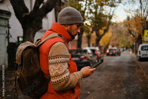 Man with backpack looking at phone on autumn street, Belgrade