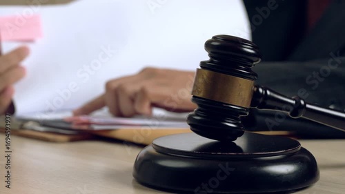 Close-up of judge gavel on desk with blurred lawyer handling documents in background, symbolizing legal authority, justice, and court decision.