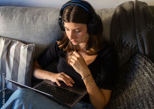 Blonde teenage girl studying online with laptop at home.Warm, modern living room atmosphere.Horizontal format, real photography