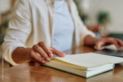 Fotografie Close up of a manager turning page of open notebook while using laptop computer