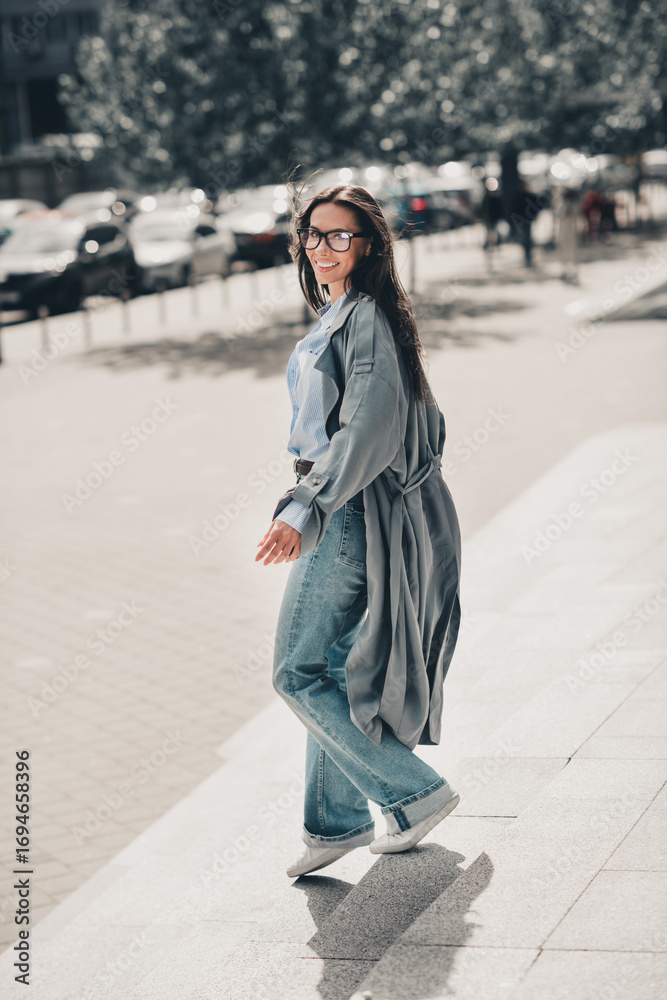 Fototapeta premium Confident woman with long brown hair walking stylishly on a city street in casual attire showcasing urban charm, vertical portrait