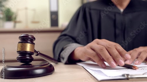 Judge signing a legal order in courtroom with traditional justice symbols including gavel and balance scale.