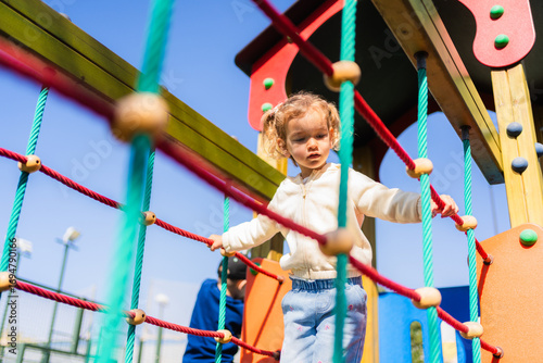 Young girl enjoying a sunny day, carefully balancing on a rope bridge at a playground