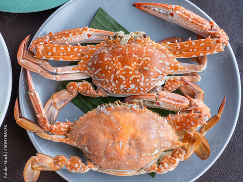Freshly steamed blue crabs served on a plate with banana leaf. Traditional Thai seafood dish with vibrant orange shells, ready to eat.