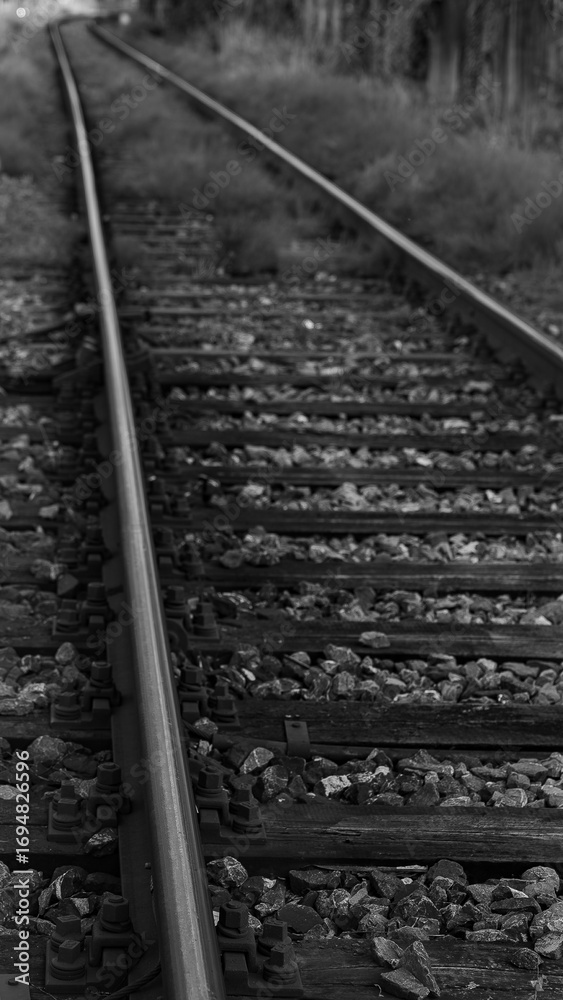 Fototapeta premium Monochrome photo of railway tracks with gravel and sleepers. Strong perspective lines create minimalist industrial art