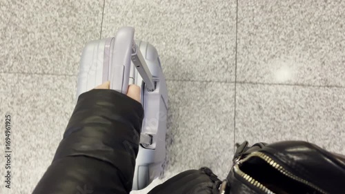 POV of walking woman holding handle of wheeled luggage suitcase, tourist or businesswoman airport arrival or departure