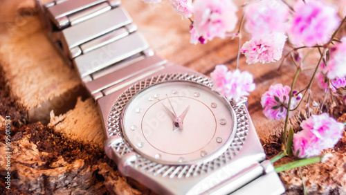 Elegante reloj plateado con flores rosas sobre superficie de madera