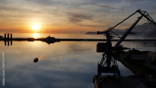Beautiful sunset in the port of Bar, Montenegro. Calm water with reflections, pilot boat moving across the port basin, and mountains in the background.