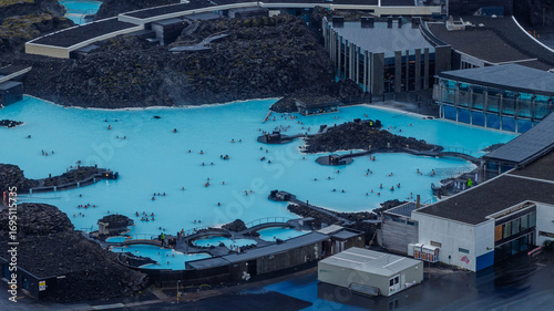 The Blue Lagoon's milky blue waters contrast with dark lava fields, featuring visitors, modern spa facilities, and rugged volcanic surroundings.