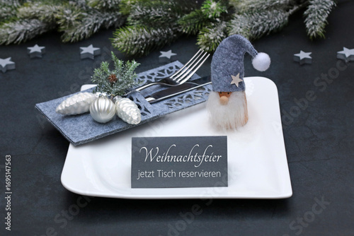 Weihnachten Reservierung: Gedeckter Tisch mit Teller, Besteck, Weihnachtsdekoration und einer Tischkarte mit der Beschriftung Weihnachtsfeier jetzt Tisch reservieren.	