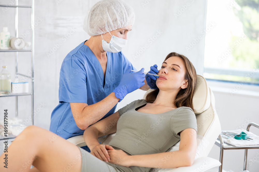 Fototapeta premium Experienced female doctor giving young woman lip filler injections at clinic