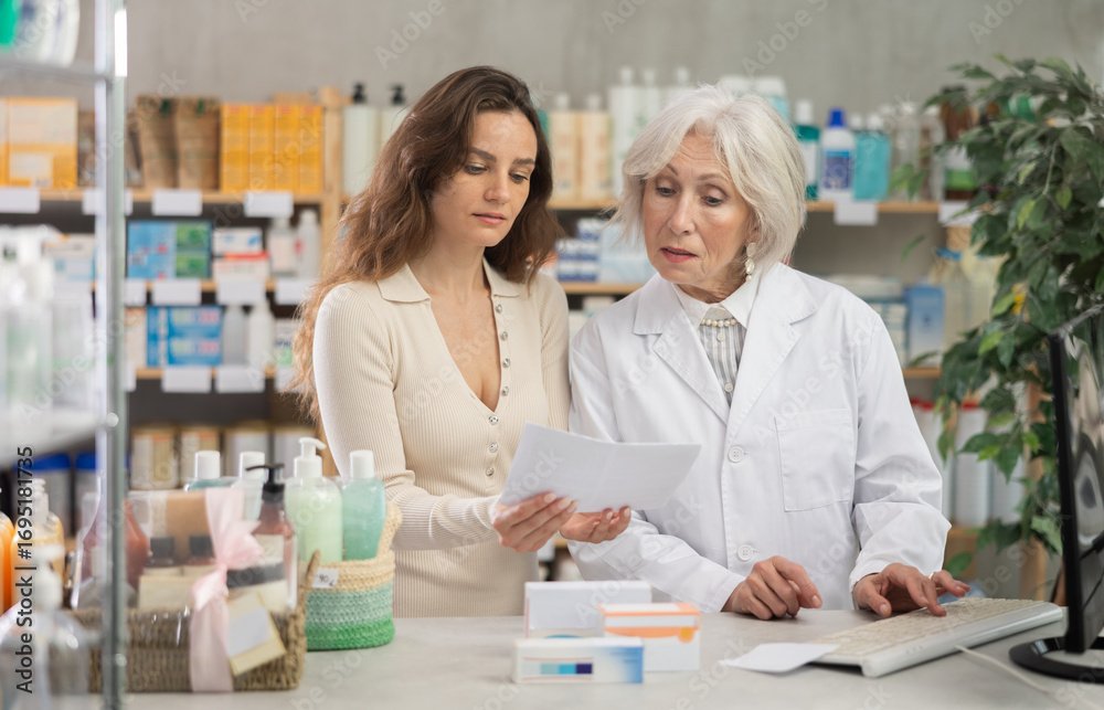 Obraz premium Senior woman pharmacist searches for a medicine from a medical prescription on a computer. Female buyer looking for cold pills and consulting a pharmacist