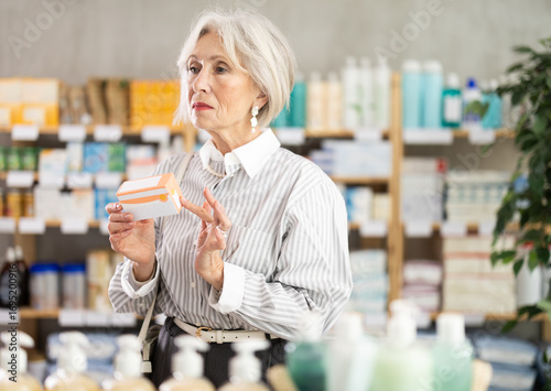 Papier peint Mature woman holds packages of paracetamol in her hands against the background of shelves with pharmacy products and medicines