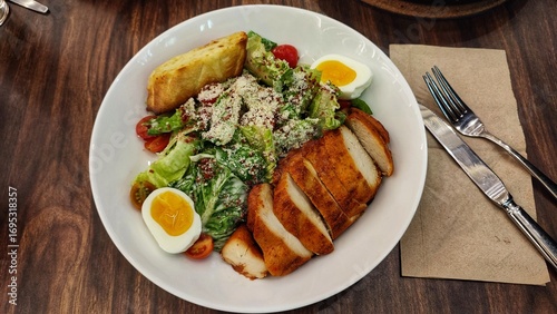 A delicious and healthy meal featuring a fresh Caesar salad with sliced grilled chicken, cherry tomatoes, and a boiled egg. The salad is topped with grated cheese.