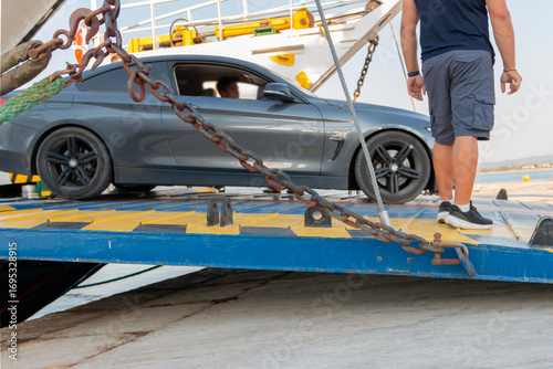Cars exiting a docked ferry, with the ferry ramp down over the water. Off- ramps lower for cars to exit at a ferry landing.
