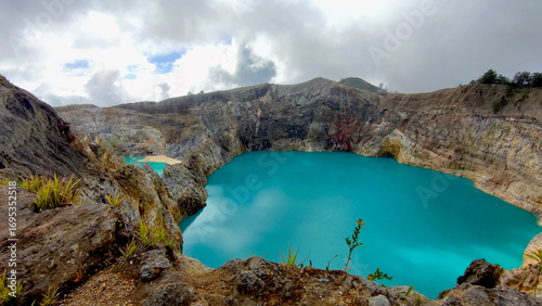 A stunning view of the Kelimutu Crater Lakes, located on the island of Flores, Indonesia. The vibrant turquoise water of the lake contrasts beautifully with the surrounding rugged, volcanic terrain.