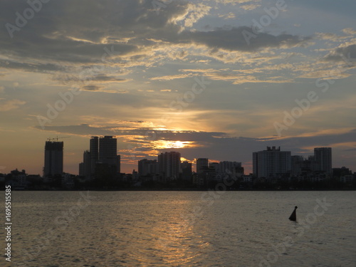 Wallpaper Mural City Skyline at Golden Hour Over Calm Lake — Sun Peeking Through Clouds, Gentle Reflections Torontodigital.ca