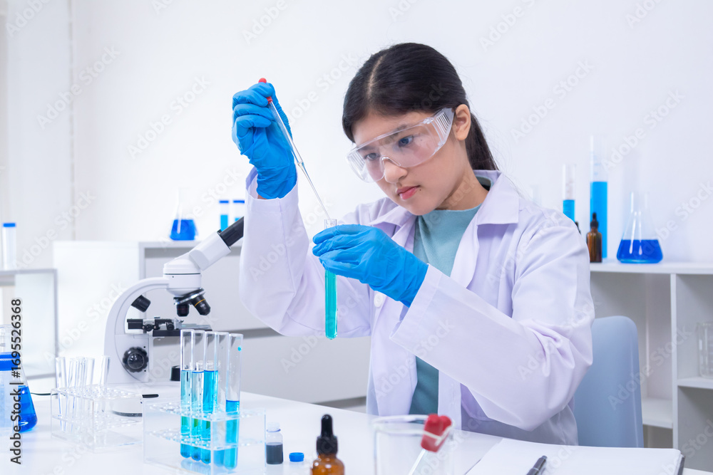 Fototapeta premium A young Asian female scientist in lab coat and gloves holds a glass pipette carefully in a science laboratory, demonstrating scientist, experiment, research, and laboratory skills.