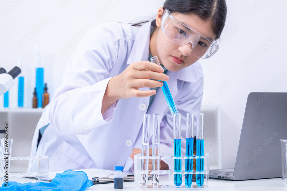 Fototapeta premium Teen scientist girl conducting science test by carefully evaluating blue solution in laboratory. Science, laboratory, experiment, and research demonstrate academic progress and practical skills.