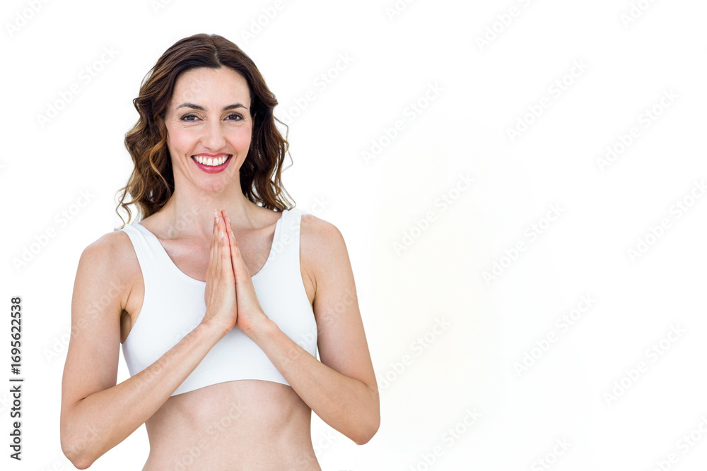 Fototapeta premium Woman smiling and holding palms together in prayer pose in studio wearing white sports bra
