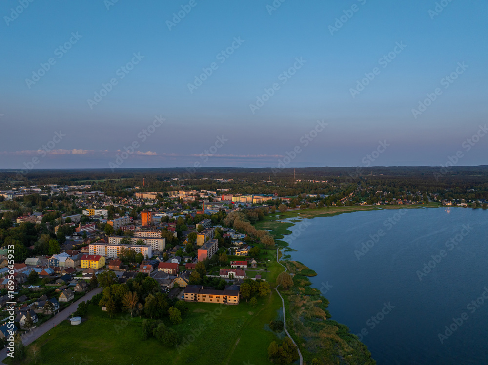 Fototapeta premium Aerial view of Võru, Estonia at sunset, featuring the serene Tamula Lake and surrounding townscape. Perfect for nature, travel, or cityscape themes with peaceful, scenic countryside vibes.