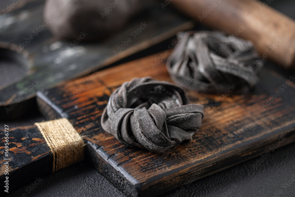 Fototapeta premium Homemade uncooked black tagliatelle noodles on a wooden board