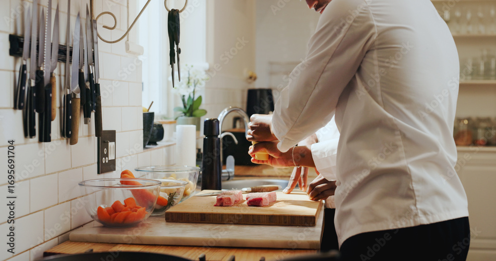 Fototapeta premium Chef hands, team and steak seasoning in kitchen for meal prep, learning recipe and enhance flavor. People, mentor and intern with spices on beef for teaching meat dinner, culinary skill and guidance