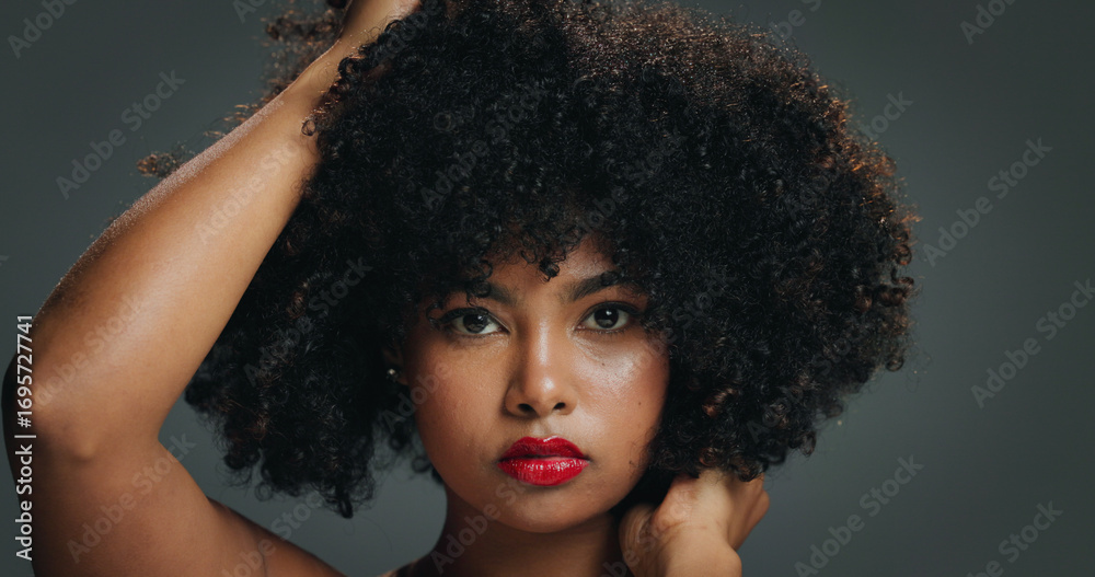 Fototapeta premium Portrait, face and woman in studio with afro, makeup and organic cosmetic for healthy curls. Proud, confident and African female person with beauty, natural hair care and lipstick on gray background