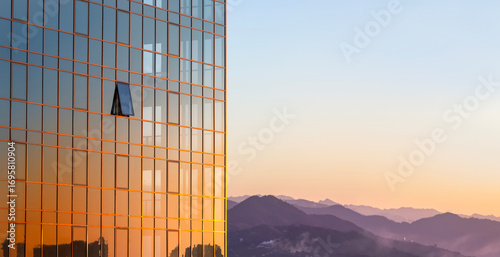 The glass wall of a modern building against the background of the sky and mountains in the rays of a golden sunset