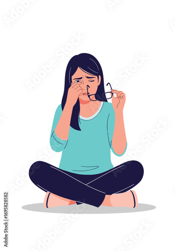 Young woman sitting cross legged crying and rubbing her eyes while holding her glasses